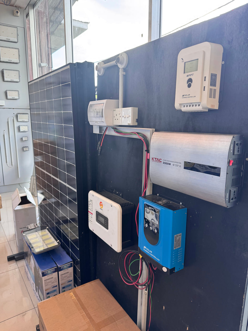 A showroom demonstration board: a framed solar panel wired through an MPPT charge controller to a wall-mounted inverter.